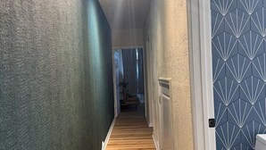 Un couloir étroit avec un escalier en bois menant à une pièce dont l’un des murs est décoré d’un motif géométrique.