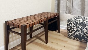 Un banc en bois avec une assise en osier tressé, un pouf à motifs et un tableau floral accroché au mur.
