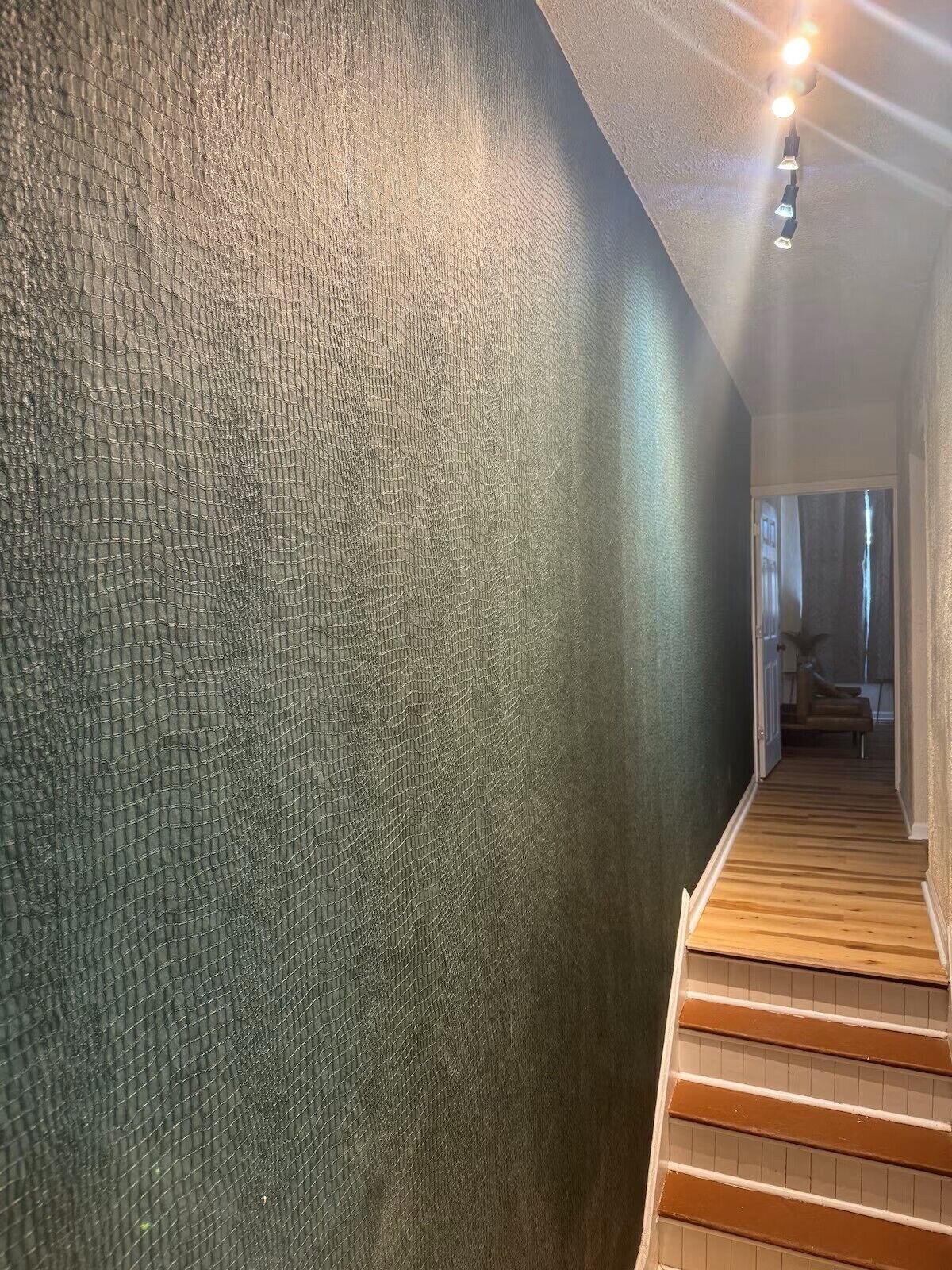 Una escalera de madera con escalones que conducen a una plataforma, una pared con textura y una lámpara en el techo.