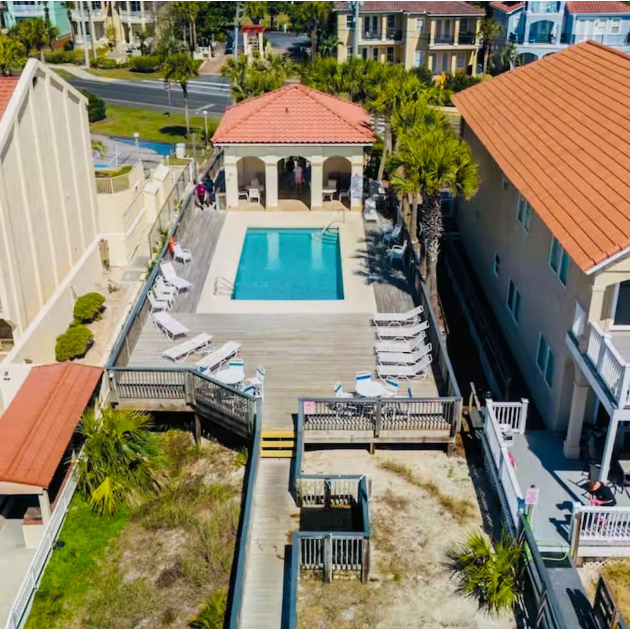 An aerial view of a hotel with a swimming pool, a covered patio area, and a boardwalk leading to the pool.
