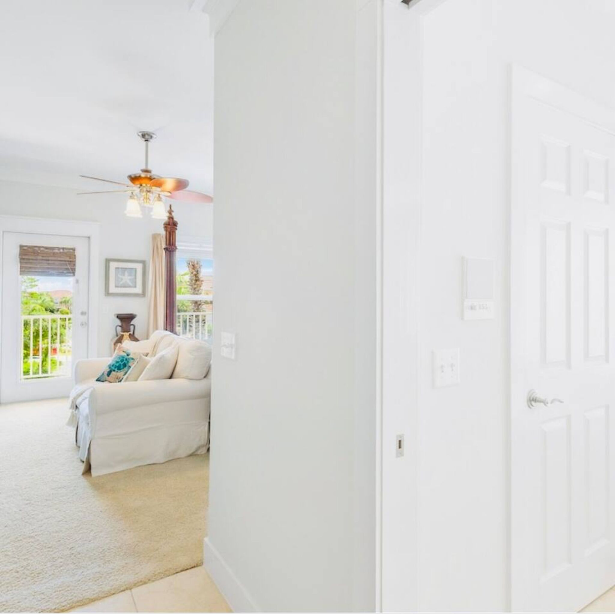 A white interior with a white door, a ceiling fan, and a white sofa with a cushion.