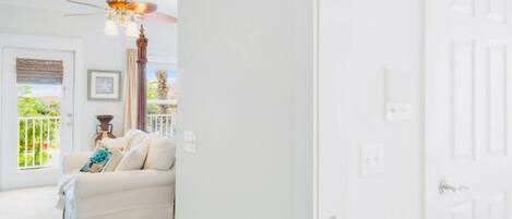 A white interior with a white door, a ceiling fan, and a white sofa with a cushion.