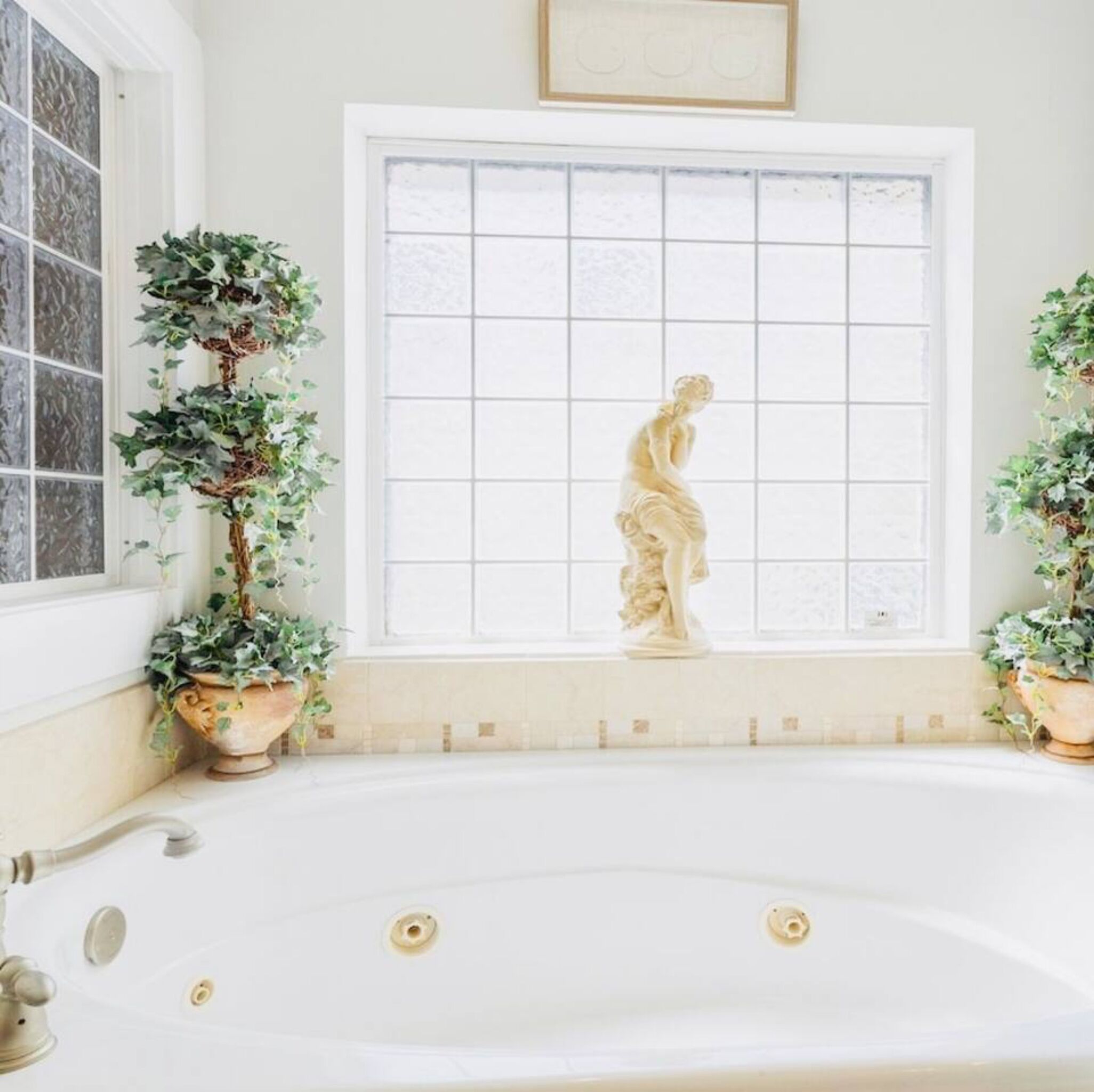 A bathroom with a bathtub, a window with a grid pattern, and two potted plants.