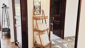 A hallway with a wooden rack holding folded towels, a painting on the wall, and patterned floor tiles. - Guesthouse Schindhard (Schindhard)
