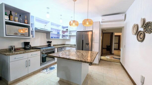 Una cocina moderna con encimeras de granito, electrodomésticos de acero inoxidable e iluminación colgante.