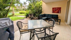 Un patio con una mesa y sillas de vidrio, una silla colgante, un sofá y un cuadro en la pared.