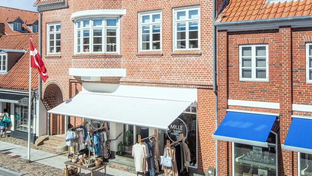 A red brick building with a white awning, a flag, and a storefront with clothing items displayed. - 2 Person Holiday Home in Ringkobing (Ringkobing)