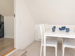 A white dining table with four blue cups and saucers, white chairs, and a grey sofa in the background.