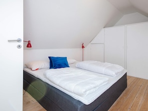A bedroom with a bed, two bedside lamps, a wardrobe, and a door.