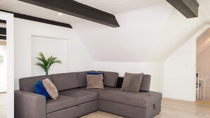 A modern living room with a sectional sofa, a potted plant, and a white door. - 2 Person Holiday Home in Ringkobing (Ringkobing)