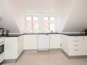 A kitchen with white cabinets, a black countertop, and a window with a view of a red-tiled roof. - 2 Person Holiday Home in Ringkobing (Ringkobing)