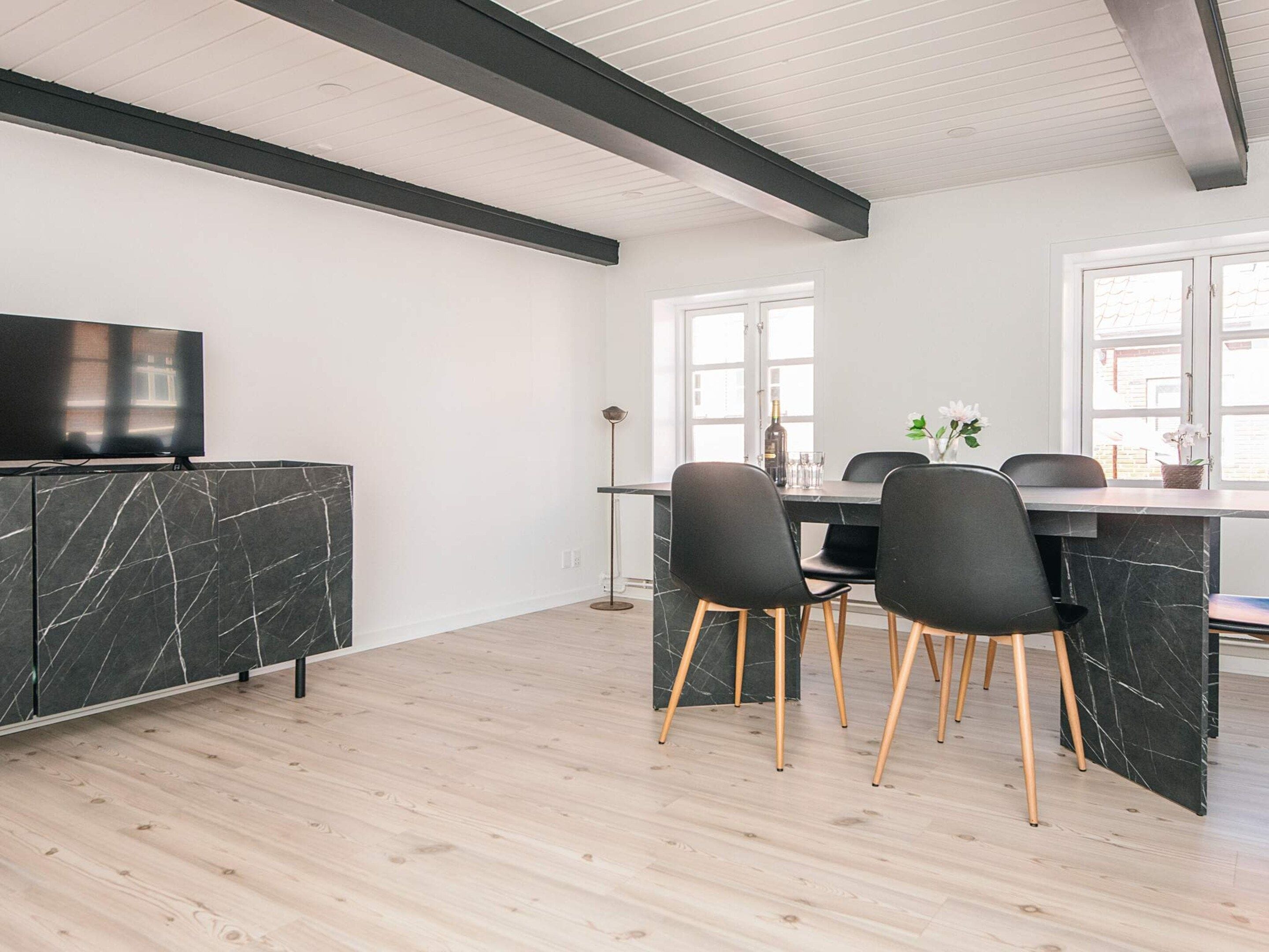 A modern kitchen with a marble countertop, black chairs, and a television.