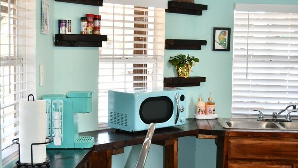A kitchen with teal walls, wooden cabinets, a microwave, a toaster, and a sink.
