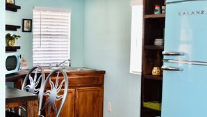 A kitchen with a blue refrigerator, wooden cabinets, a dining table with chairs, a microwave, and a window with blinds.