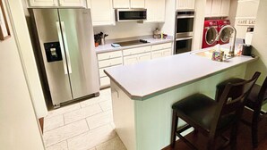 Une cuisine moderne avec des meubles blancs, des appareils en acier inoxydable et un îlot central doté de tabourets de bar.
