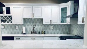 A modern kitchen with white cabinetry, a marble countertop, and three white bar stools.