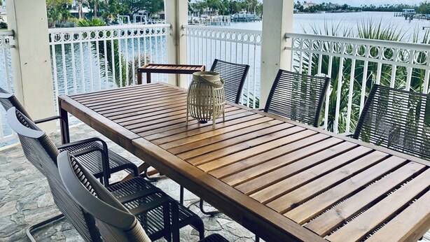 A wooden table with chairs and a lantern on a balcony overlooking a body of water.