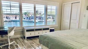 A bedroom with a bed, a desk, and a window overlooking a water body.