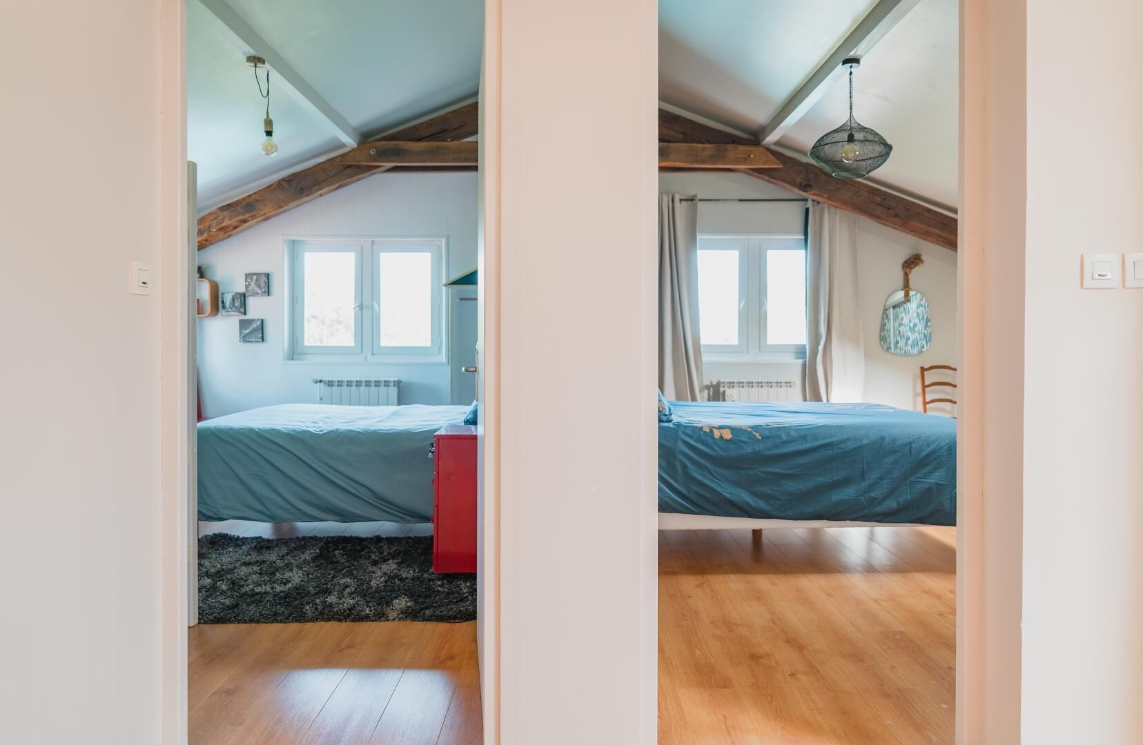 A bedroom with a bed, a red dresser, a window, and a ceiling with exposed beams.