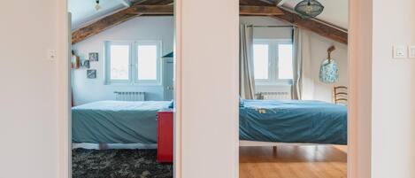 A bedroom with a bed, a red dresser, a window, and a ceiling with exposed beams.
