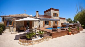 Eine Villa mit Swimmingpool, Sitzgelegenheiten im Freien und einer Steinaußenfassade.