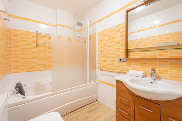 Un baño con bañera, ducha, lavamanos y tocador de madera.