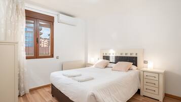 Een slaapkamer met een bed, nachtkastjes, een raam met gordijnen en een airconditioning.