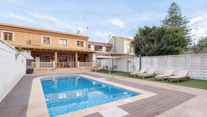 Una piscina con sillas de descanso, un patio y una casa con techo de tejas.
