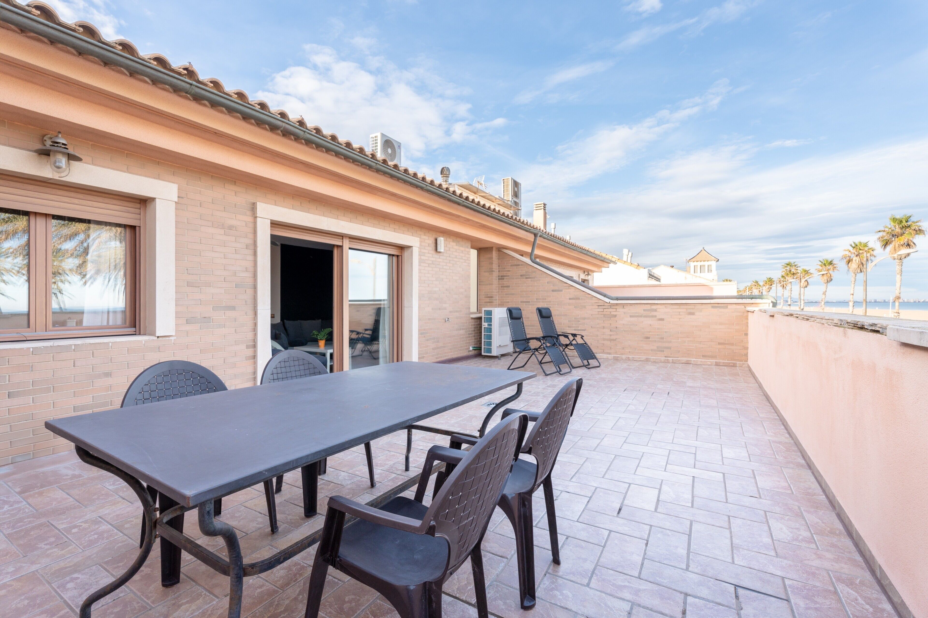 Un patio exterior con una mesa y sillas, un muro de ladrillo y vista al mar.