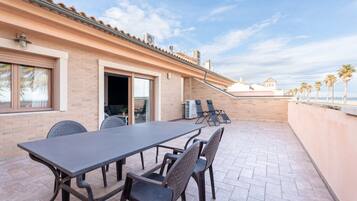 Un patio exterior con una mesa y sillas, un muro de ladrillo y vista al mar.