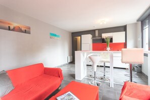 Un soggiorno moderno con un divano rosso, un tavolino e un angolo cottura con isola bianca e sgabelli da bar.