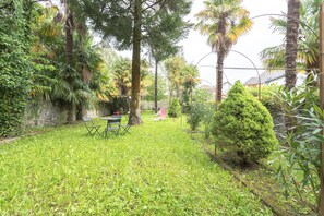 Ein üppiger Garten mit einem kleinen Tisch und Stühlen, umgeben von verschiedenen Bäumen und Sträuchern.