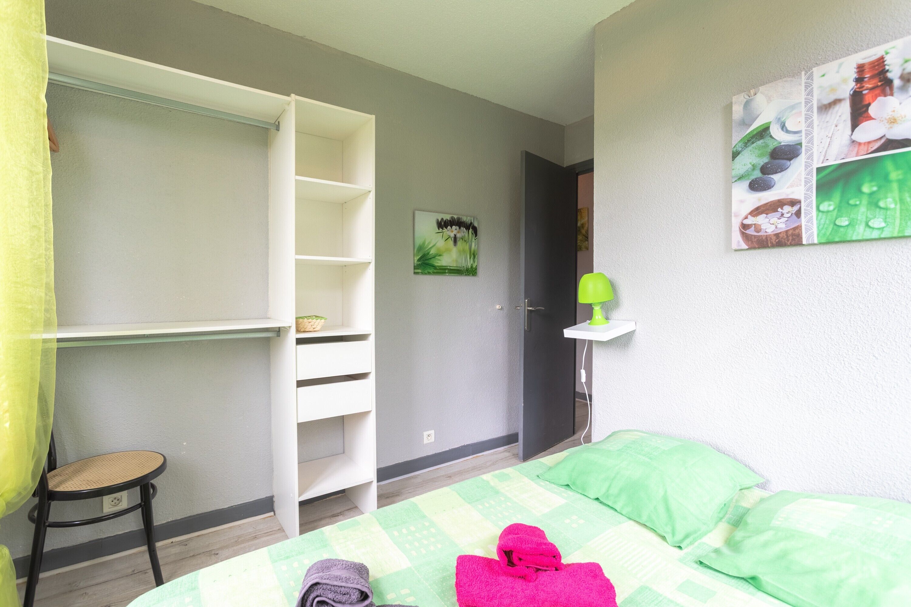 Un dormitorio con una cama, una colcha verde y blanca a cuadros, una almohada verde y un armario blanco, además de un taburete pequeño.