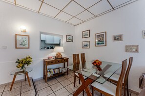 Un comedor con una mesa de vidrio, sillas de madera, una mesita auxiliar con un florero y una estantería.