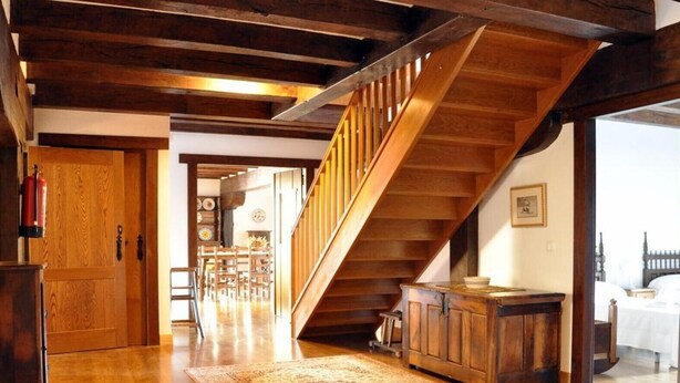 A wooden staircase leading to an upper level, a wooden door, a dining area with chairs and a table, and a patterned rug on the floor.
