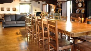 A dining area with a long wooden table and chairs, a sofa, and a kitchen area with decorative plates.