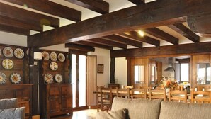 A spacious living area with exposed wooden beams, a sofa, a dining table with chairs, and a wall decorated with plates.