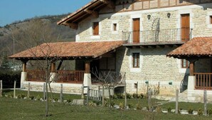 Un edificio in pietra su due piani con un balcone, un portico coperto e montagne sullo sfondo.