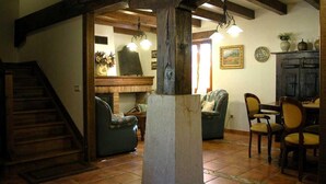 A spacious living area with a fireplace, wooden beams, a staircase, and a dining area with chairs and a table.