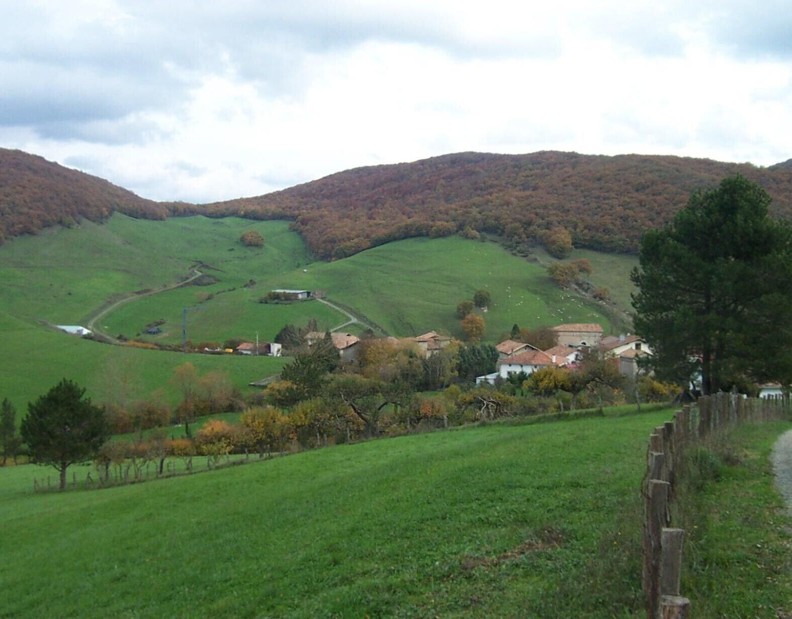Paisaje rural con colinas ondulantes, un pequeño pueblo y una valla de madera.