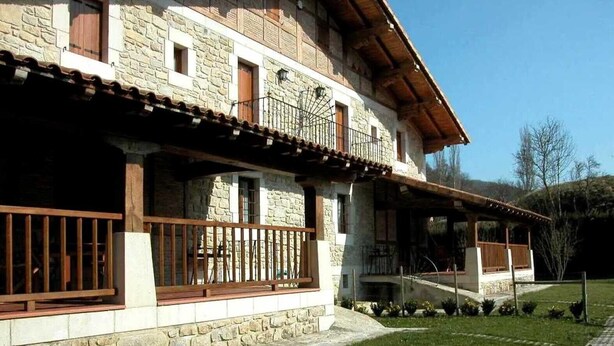 A stone building with a balcony, a grassy yard, and a clear sky.