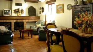 A living room with a fireplace, wooden beams, a television, and a dining area with chairs and a table.