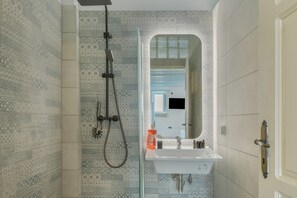 A bathroom with patterned tiles, a shower, a sink with toiletries, and a mirror. - Apartment 'For Two' with Balcony and Wi-Fi (Astypalaia)