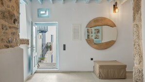 A hallway with a stone wall, a wooden bench, a round mirror, and a door leading to a staircase.