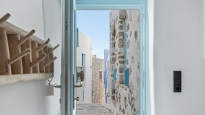 A narrow alleyway with a wooden rack and a door leading to a building with stone walls and blue shutters.