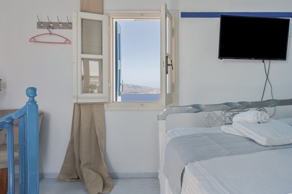 A bedroom with a bed, a TV, a window with a view, and a coat rack.