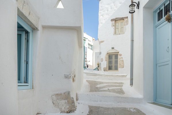 A narrow street with white buildings, blue doors, and a clear sky.