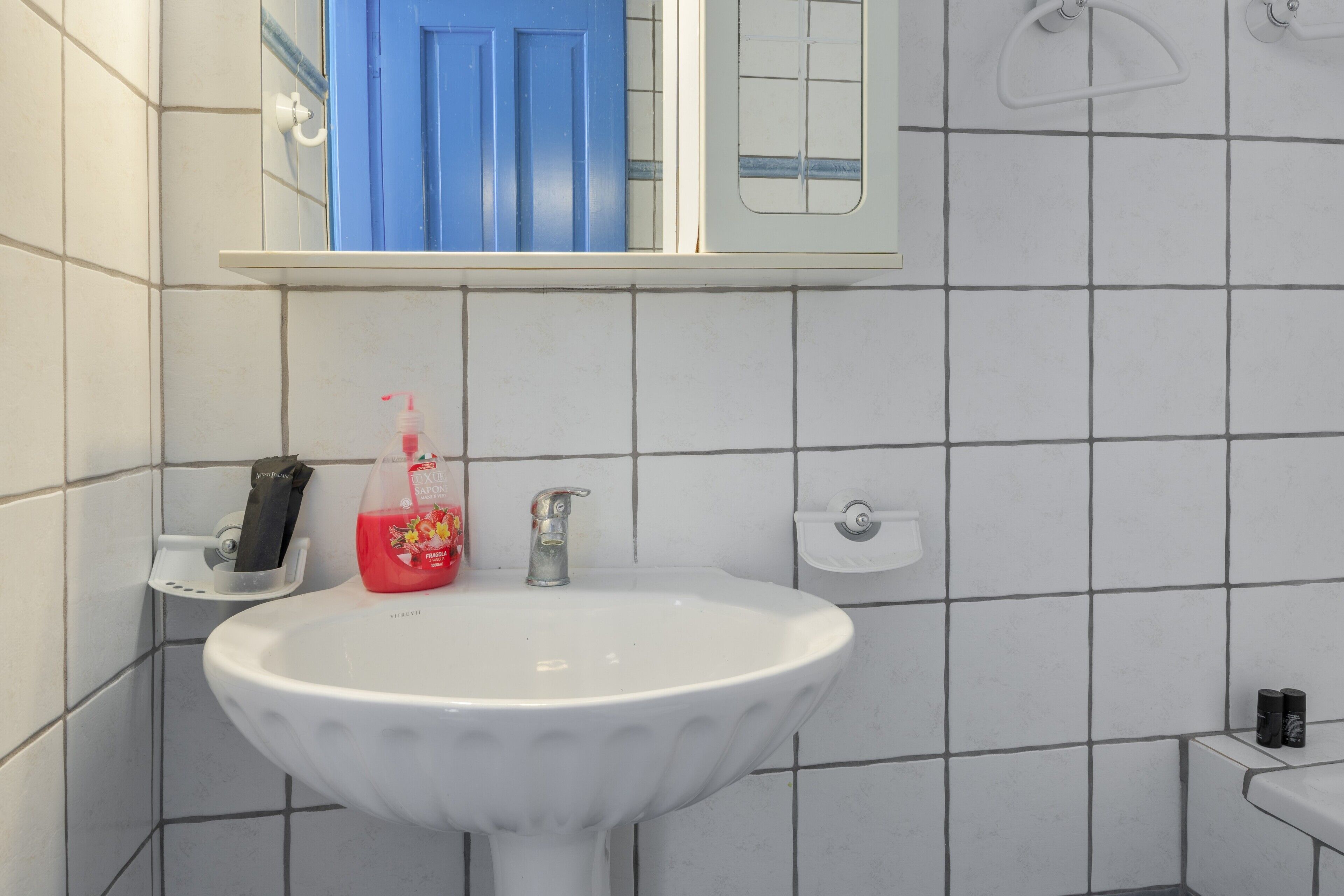 Um banheiro com pia branca, porta azul e suporte para toalhas branco.