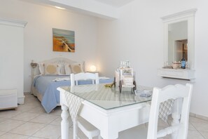 A bedroom with a bed, a bedside table with a lamp, a glass table with chairs, a dresser, and a mirror.