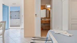A hotel room with a bed, a bathroom with a mirror and sink, a chair, and a view of buildings outside. - Apartment 'Sea View Studio' with Sea View, Wi-Fi and Air Conditioning (Astypalaia Town)